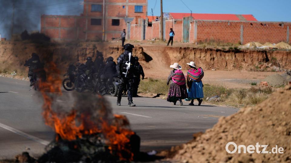 Anwohner gehen an einem Polizisten vorbei, der in Bolivien an einer brennenden Barrikade steht. Bild: Juan Karita/AP/dpa