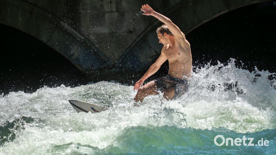 Patrick surft bei sommerlichen Temperaturen mit seinem Board auf der Eisbachwelle im Englischen Garten in München. Bild: Peter Kneffel/dpa