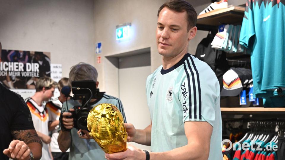 Lächelnd signiert Manuel Neuer einen goldenen WM-Pokal. Bild: Federico Gambarini/dpa