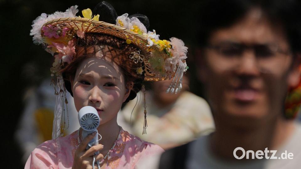 Eine Frau, die einen Hut mit Blumen und ein traditionelles Kostüm trägt, kühlt sich mit einem tragbaren elektrischen Ventilator ab, während Menschen an einem heißen Tag die Verbotene Stadt in Peking besuchen. Bild: Andy Wong/AP/dpa