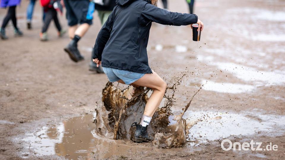 Eine Besucherin des Open-Air-Festivals „Rock im Park“ springt in eine Pfütze. Bild: Daniel Karmann/dpa