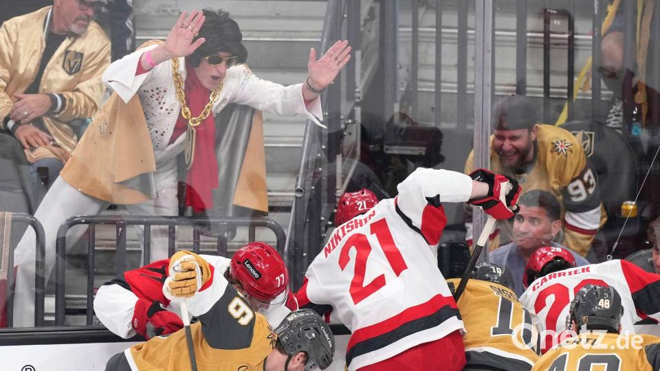Ein Elvis-Imitator schlägt auf die Scheibe, während die Spieler um den Puck kämpfen. Bild: Candice Ward/AP/dpa