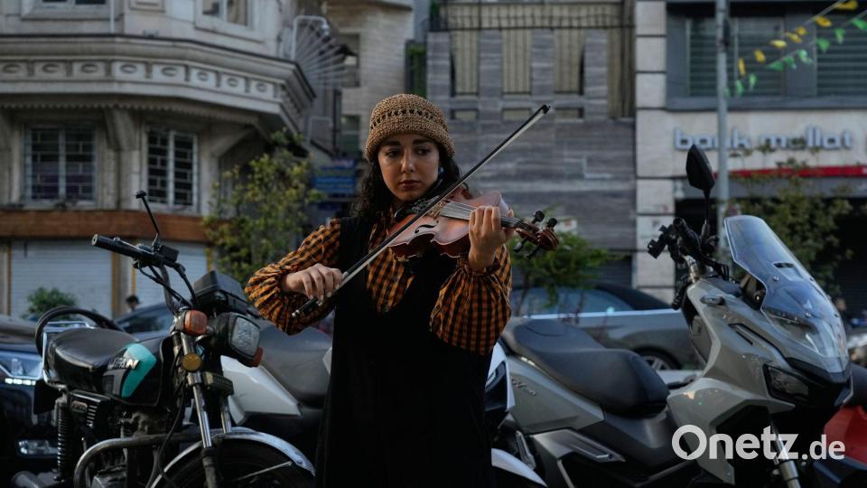 Eine Straßenmusikerin spielt Geige auf einem Bürgersteig im Norden Teherans. Bild: Vahid Salemi/AP/dpa