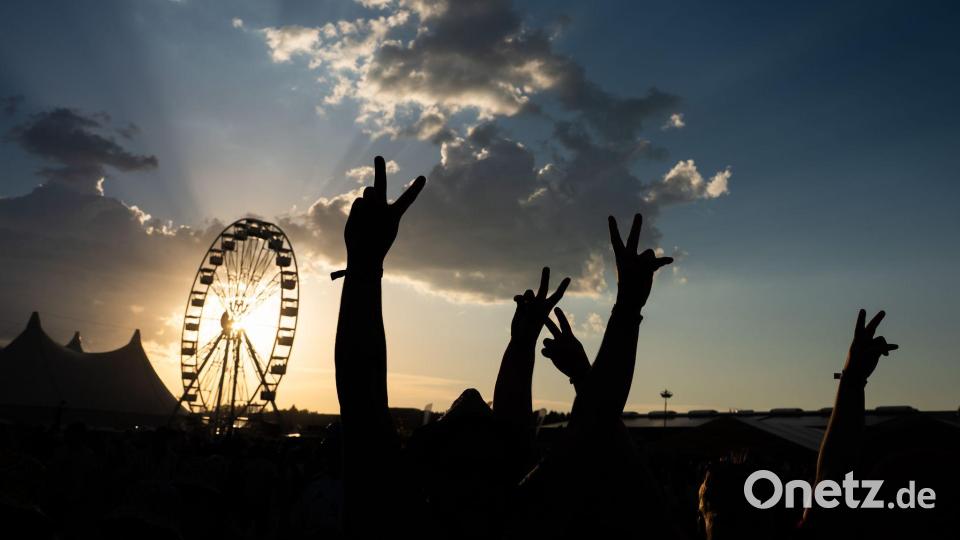 Festivalbesucher halten bei Sonnenuntergang ihre Hände auf dem Southside in die Höhe und sind dabei als Silhouette zu sehen. Bild: Silas Stein/dpa