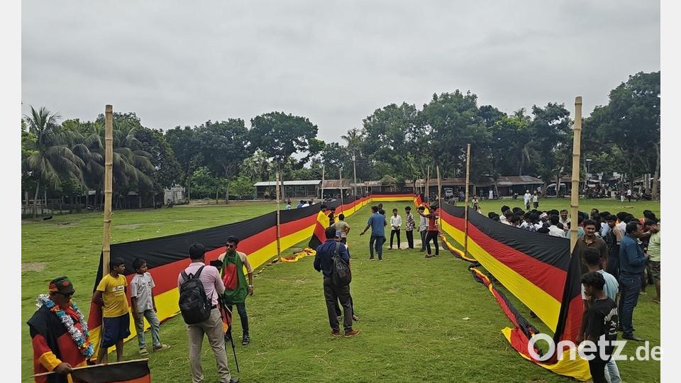 Fans haben sich an einer Seite versammelt, während eine riesige, 7,5 Kilometer lange deutsche Flagge auf dem Schulplatz von Nishchintapur im bangladeschischen Distrikt Magura entrollt wurde. Bild: Nazrul Islam/Nerob Hossain/dpa