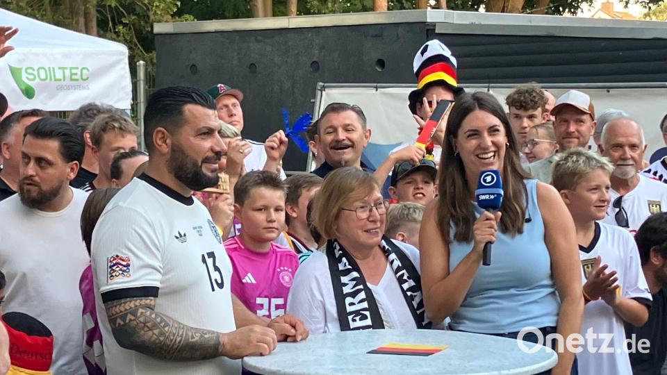 Gruß aus Undavs Heimat Achim nach East Rutherford: Edeltraut Koch (M), erste Trainerin von Deniz Undav, und Aykut Kaldirici (l), Trainer der 1. Herren des TSV Achim und eng befreundet mit Undavs Familie bei einer Schalte mit ARD-Reporterin Anna Klär. Bild: Claas Henning/dpa