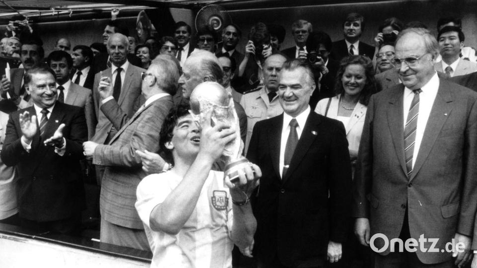 29.6.1986: Der argentinische Fußballstar Diego Maradona jubelt mit dem eroberten Weltmeisterschaftspokal - der mexikanische Staatspräsident Miguel de la Madrid (2. von rechts) und Bundeskanzler Helmut Kohl (rechts) schauen zu. (Archivbild) Bild: dpa/Picture-Alliance/dpa