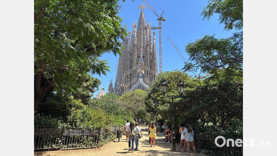 Touristen suchen bei großer Hitze den Schatten auf der Placa de la Sagrada Familia vor der gleichnamigen Basilika in Barcelona. (Archivbild) Bild: Jan Uwe Ronneburger/dpa