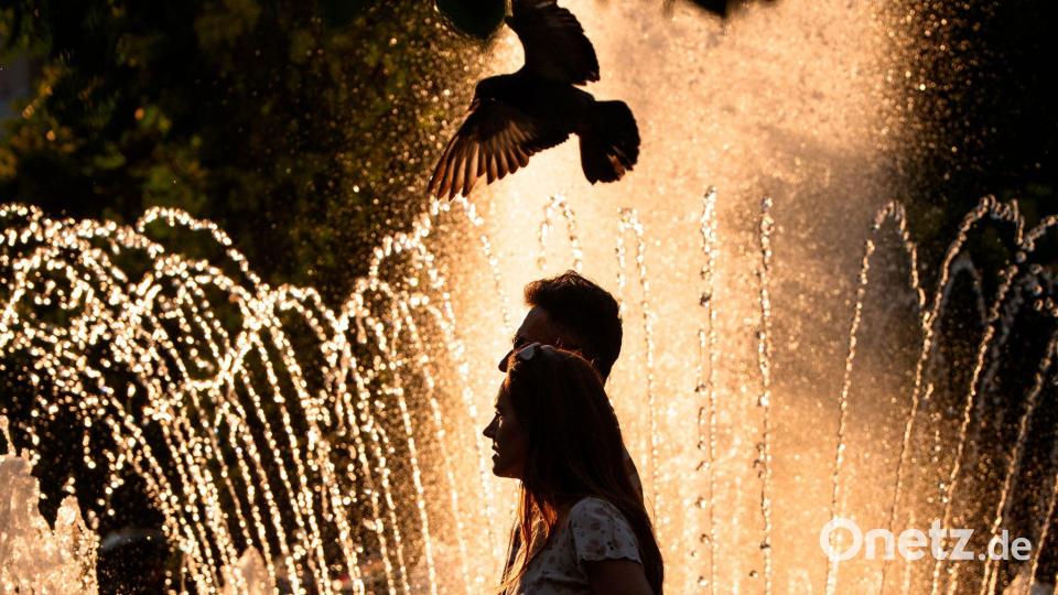 Ein Paar geht an einem Springbrunnen in Bukarest vorbei, während der nationale Wetterdienst für Teile des Landes in den kommenden Tagen eine Hitzewarnung der Stufe „Rot“ herausgegeben hat. Bild: Andreea Alexandru/AP/dpa