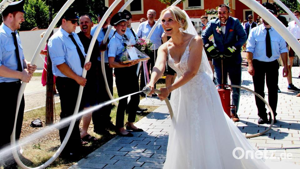 Mit Wasser aus der Kübelspritze der Feuerwehr bot Braut Janine Dorn einigen Gästen eine kurzzeitige Abkühlung bei mehr als 30 Grad Hitze an ihrem Hochzeitstag. Und Ehemann Florian sorgte im Hintergrund pumpend für den Wasser-Nachschub. Bild: Leonhard Ehras