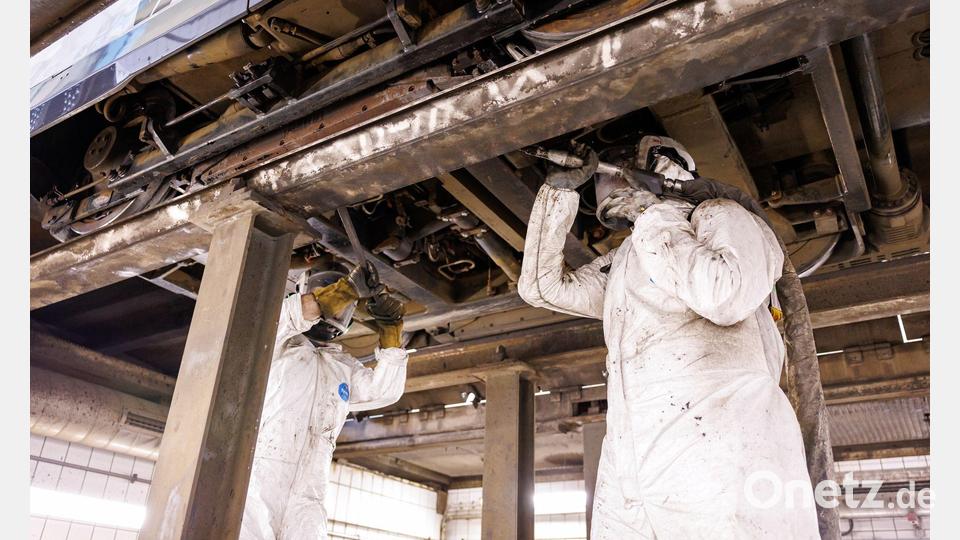 Mitarbeiter der Werkstatt der Verkehrsaktiengesellschaft VAG zeigen, wie ein Trockeneisstrahlgerät angesetzt werden muss, um ein durch Bitum verschmutztes Fahrwerks einer Straßenbahn zu reinigen (gestellte Szene). Bild: Daniel Karmann/dpa