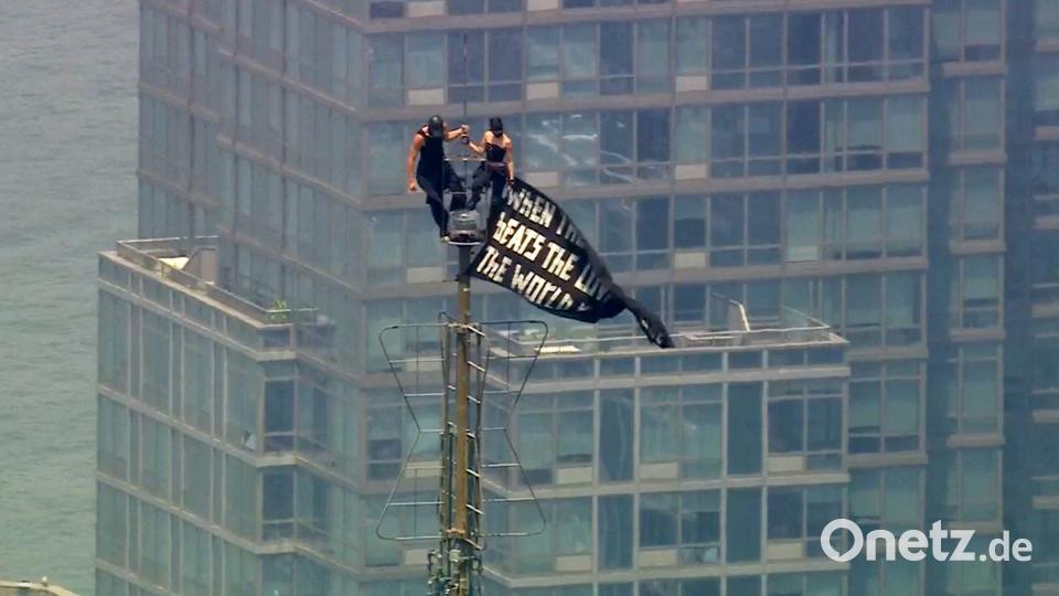 Zwei Menschen stehen auf der Spitze der Antenne des Empire State Building mit einem Banner. Bild: Uncredited/WABC-TV/AP/dpa
