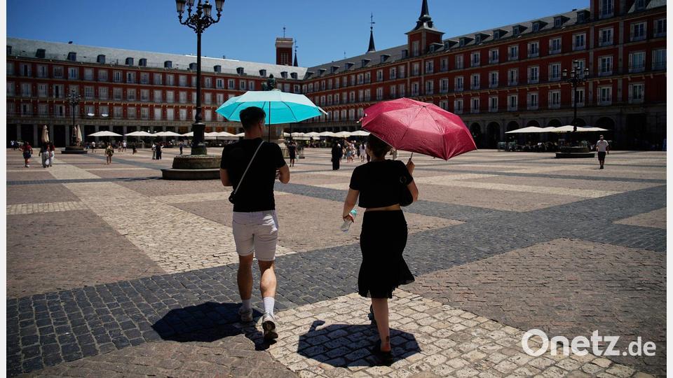 Touristen schützen sich vor der Sonne mit Regenschirmen während eines Spaziergangs durch die Stadtmitte. Bild: Andrea Comas/AP/dpa
