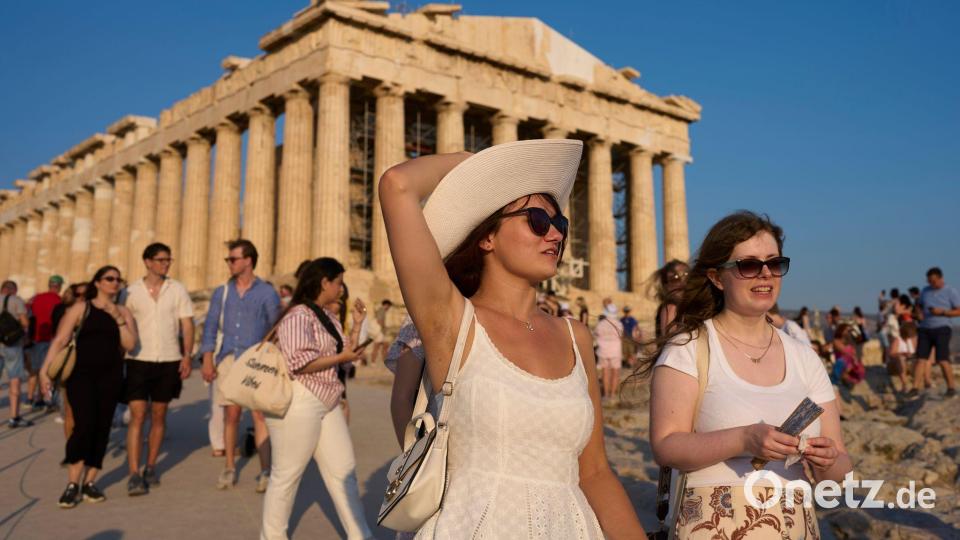 Touristen gehen an einem heißen Tag am antiken Parthenon-Tempel auf dem Akropolis-Hügel vorbei. Bild: Petros Giannakouris/AP/dpa