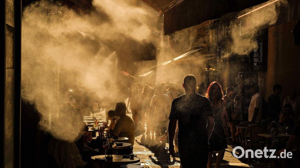 Menschen laufen unter Sprinklern eine Straße in Nizza entlang während einer Hitzewelle an der französischen Riviera. Bild: Valery Hache/AFP/dpa