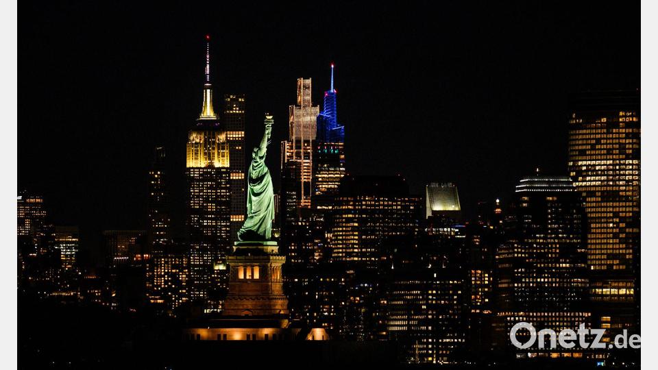 Die Freiheitsstatue steht bei Nacht vor der Skyline von Manhatten. Bild: Tom Weller/dpa