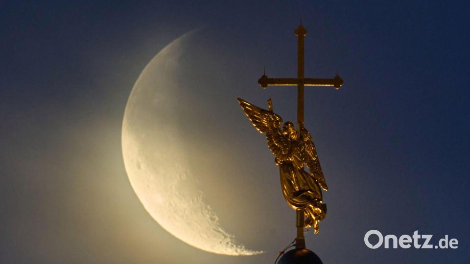 Vor dem Mond ist das Wahrzeichen der Stadt St. Petersburg, eine Wetterfahne in Form eines Engels, zu sehen. Bild: Dmitri Lovetsky/AP/dpa