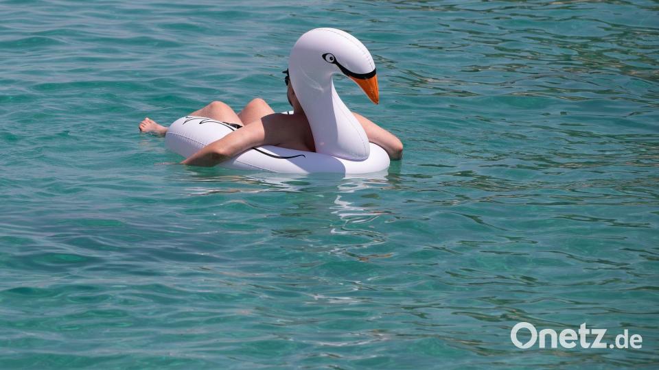 Ein Mann lässt sich auf einem Schwimmtier am Strand von Cala Vinyes auf Mallorca im türkisblauen Wasser treiben. Bild: Clara Margais/dpa