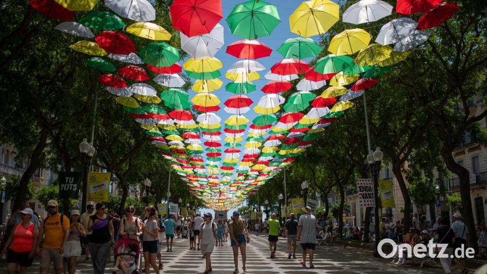 Menschen gehen eine Straße entlang, über der Schirme aufgehängt sind. (Archivbild) Bild: Laia Solanellas/EUROPA PRESS/dpa