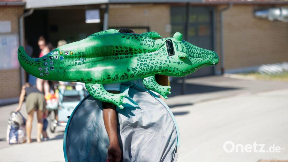 Ein Mann geht mit einem grünen Schwimm-Krokodil in ein Schwimmbad in Baden-Württemberg. Bild: Thomas Warnack/dpa