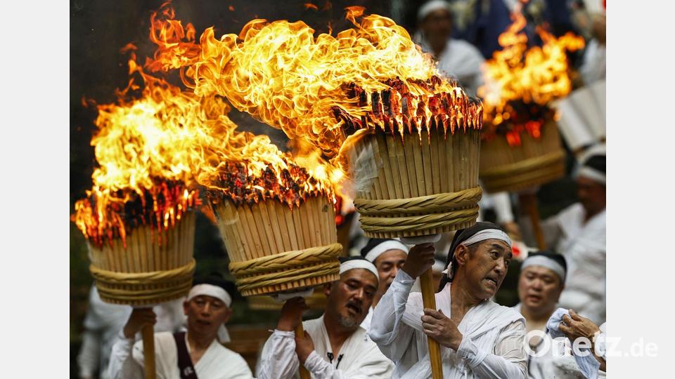 Teilnehmer tragen bei einem traditionellen Feuerfest in Japan riesige Fackeln. Bild: -/kyodo/dpa