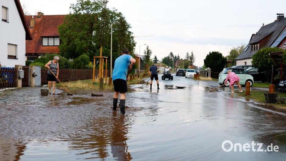Anwohner versuchen nach einem schweren Gewitter in Erlangen die Wassermassen von der Straße zu schieben. Bild: News5 / David Oßwald/NEWS5/dpa