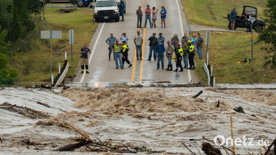 Menschen stehen zusammen und beobachten, wie der Perdenales River die Ranch Road 1623 in in Texas überflutet. Bild: Mikala Compton/Austin American-Statesman/AP/dpa