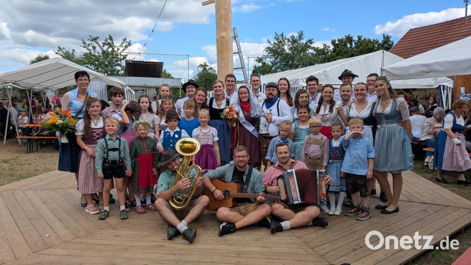 Bei der 14. Steiningloher Stodlkirwa tanzten 18 Kinder und sieben Kirwapaare um den 30 Meter hohen Kirwabaum. Als Oberkirwapaar wurden Sophia Pfab und Jonas Weiß (Bildmitte mit Blumenstrauß bzw. Kirwaliesl) ermittelt. Links hinten: Tanzlehrerin Eva Pfab, die seit zehn Jahren die Tänze einstudiert. Vorne das Trio „D’Allerscheynst’n“, das beim Austanzen aufgespielt hat. Bild: Christian Summer