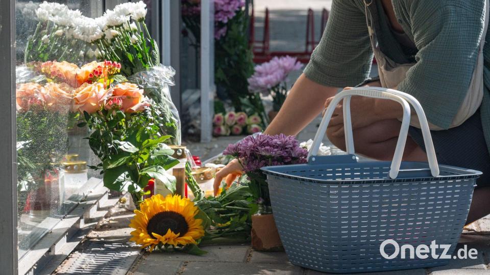 Eine Frau legt eine Karte zu Blumen und Kerzen, die vor der Bankfiliale abgelegt wurden. Nach der tödlichen Messerattacke in einer Regensburger Bank versucht die Kriminalpolizei weiter, die Hintergründe aufzuklären. Bild: Armin Weigel/dpa