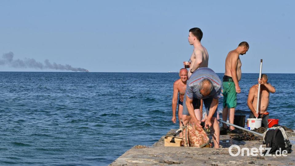 Menschen in Odessa sonnen sich, während am Horizont im Schwarzen Meer der brennende Getreidetransporter „Golden Leo“ zu sehen ist. (Archivbild) Bild: Michael Shtekel/AP/dpa
