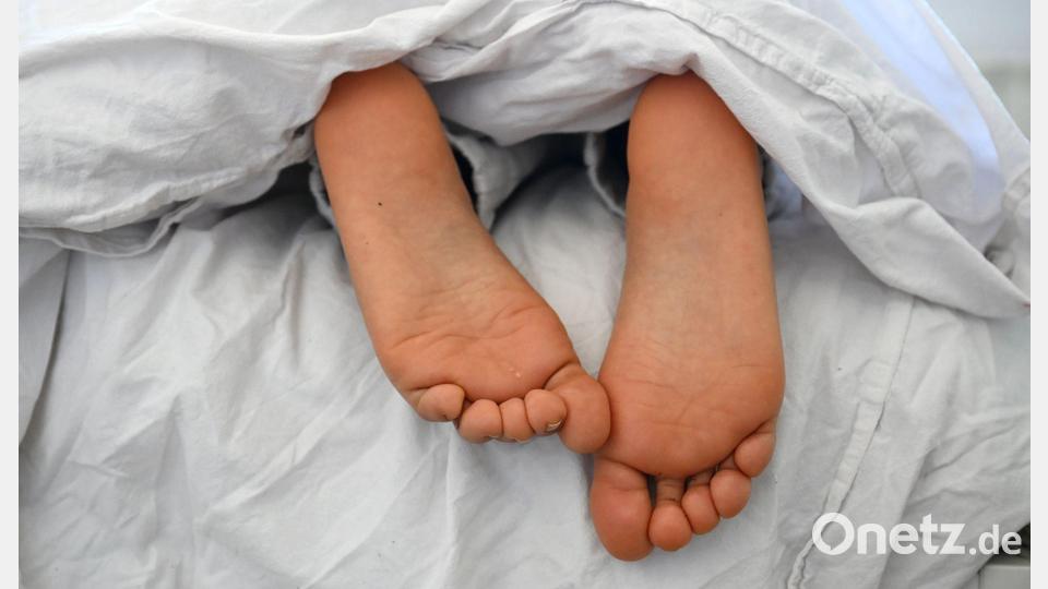 Die nackten Füße und Pyjamahose einer Frau sind unter einer Bettdecke zu sehen. Bild: Elisa Schu/dpa