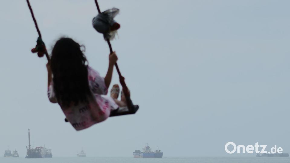 Ein Mädchen schaukelt am Ufer, während Frachtschiffe und andere Handelsschiffe in der Straße von Hormus vor Anker liegen. (Archivbild) Bild: Razieh Poudat/ISNA/AP/dpa