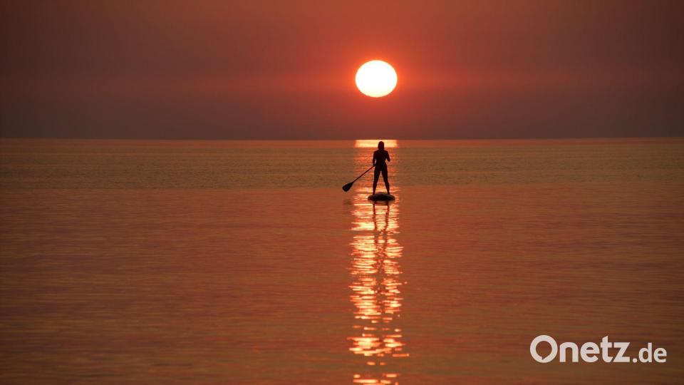 Ein Urlauber steuert bei Sonnenuntergang vor der Küste von Jantarny dem früheren ostpreußischen Palmnicken, einem Ferienort in der westrussischen Region Kaliningrad, ein Stand-up-Paddleboard. Bild: Alexander Zemlianichenko/AP/dpa