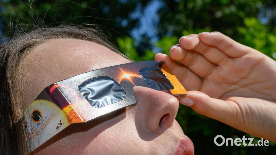 Eine junge Frau schaut durch eine Sonnenfinsternisbrille und betrachtet die Mittagssonne. Bild: Patrick Pleul/dpa