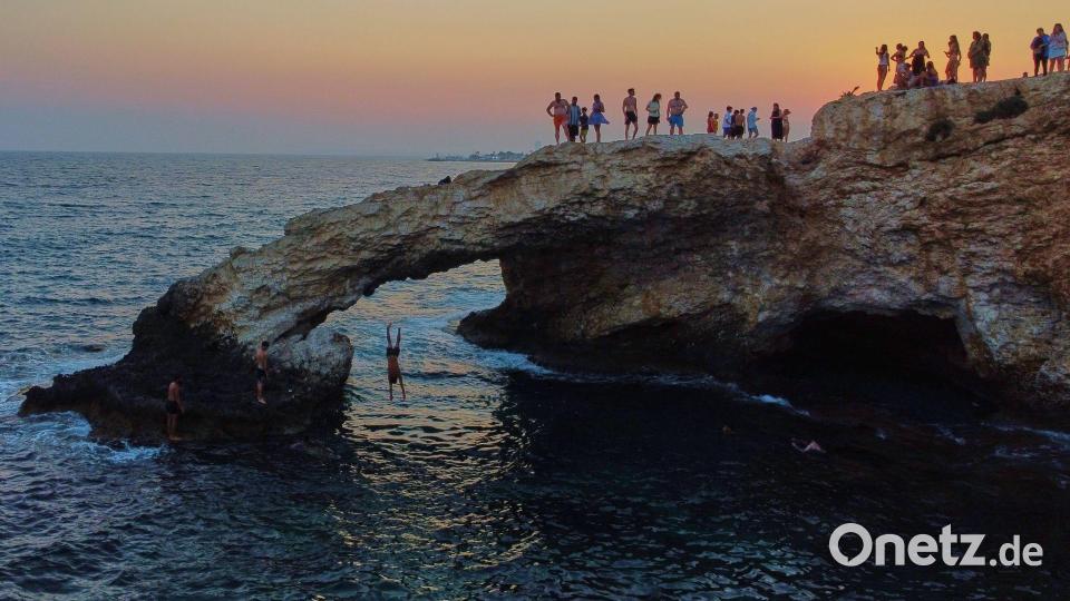 Ein junger Mann springt bei Sonnenuntergang im Ferienort Ayia Napa auf der im östlichen Mittelmeer gelegenen Insel Zypern von der natürlichen "Liebesbrücke" ins Meer. Bild: Petros Karadjias/AP/dpa