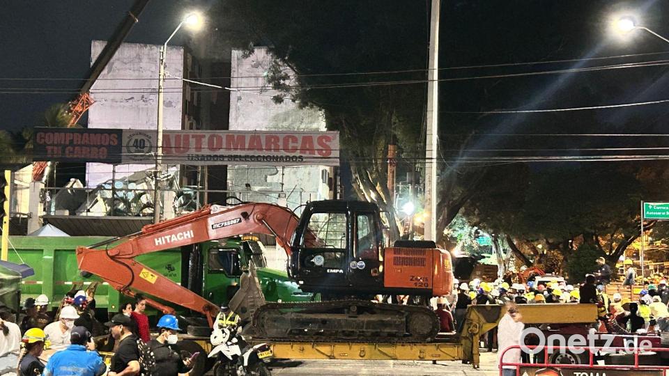 Helfer bringen einen Bagger zu einem eingestürzten Gebäude. Bild: Philipp Znidar/dpa