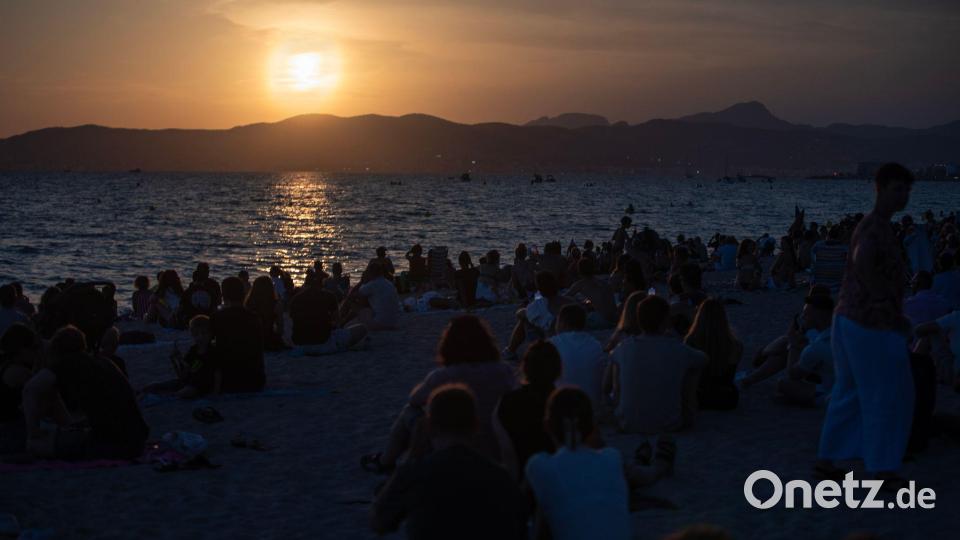 Menschen sitzen am Strand von Palma und warten auf die totale Sonnenfinsternis. Bild: Clara Margais/dpa