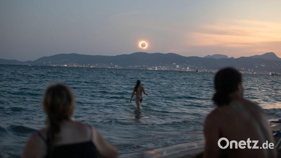 Eine Frau badet im Meer und weitere beobachten die totale Sonnenfinsternis am Strand von Palma. Bild: Clara Margais/dpa