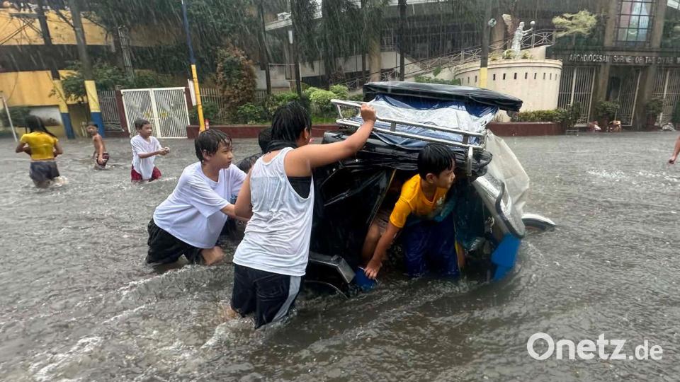 Monsunregen: Menschen schieben ein Dreirad-Taxi durch eine überflutete Straße auf den Philippinen. Bild: Joeal Calupitan/AP/dpa