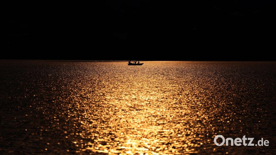 Angler rudern in einem Kahn über den im Sonnenuntergang glitzernden Hopfensee. Bild: Karl-Josef Hildenbrand/dpa