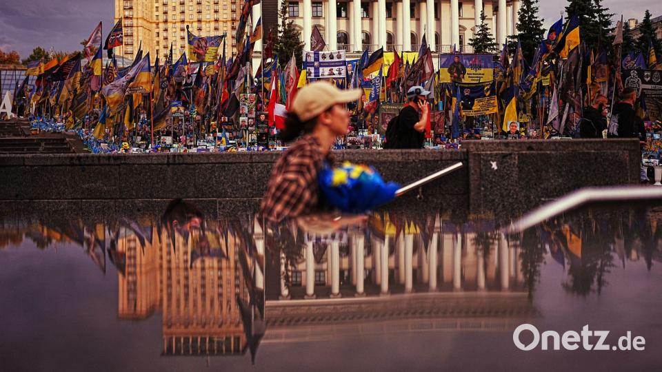 Die Nationale Musikakademie (r) spiegelt sich in einem U-Bahn-Eingang am Unabhängigkeitsplatz in Kiew wider, wo ukrainische Flaggen und Fotos zum Gedenken an die im Krieg mit Russland getöteten Zivilisten und Soldaten aufgestellt sind. Bild: Francisco Seco/AP/dpa