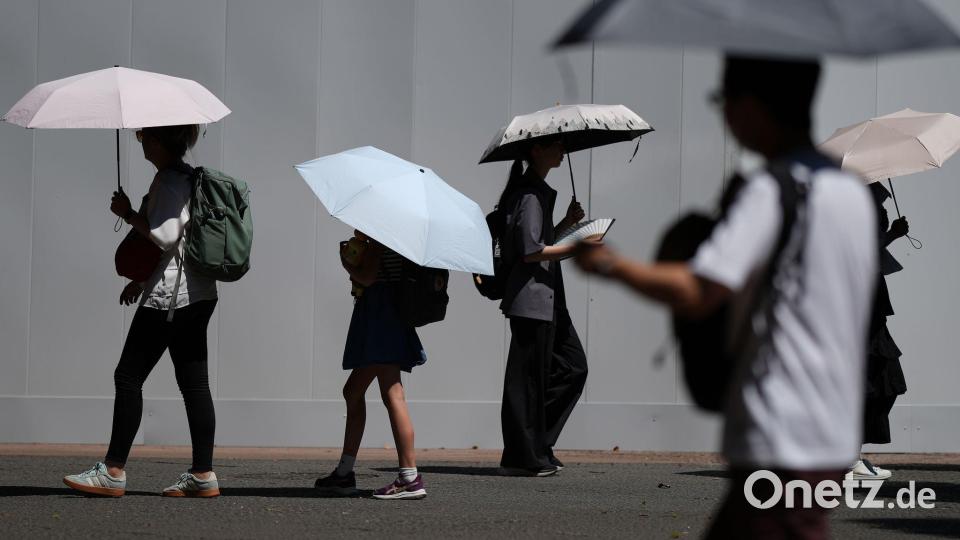 Mit Schirmen schützen sich Menschen vor der sengenden Sonne in Tokio. Bild: Eugene Hoshiko/AP/dpa