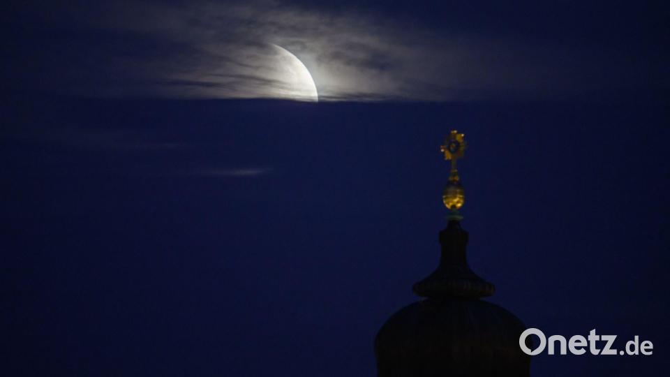 Der Mond geht am Morgen während einer partiellen Mondfinsternis hinter dem Kreuz der Frauenkirche unter. Bild: Robert Michael/dpa