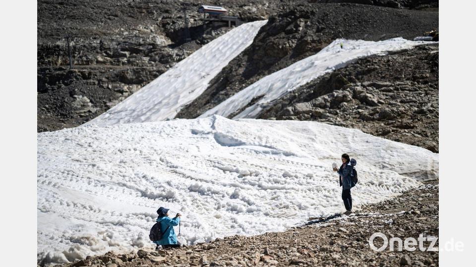 Touristen fotografieren in den Schweizer Alpen Schneereste an einer Skipiste. Bild: Gian Ehrenzeller/KEYSTONE/dpa
