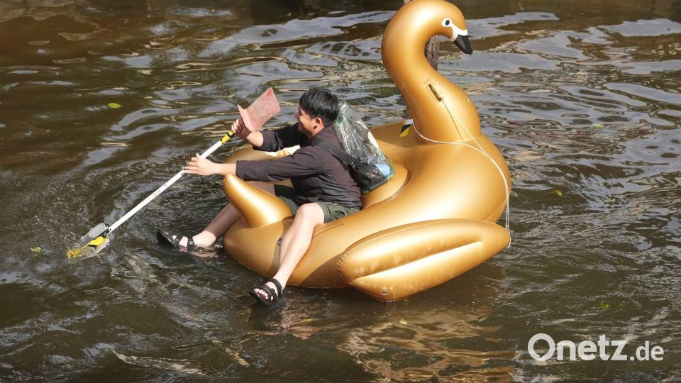 Ein Mann paddelt nach tagelangen starken Regenfällen auf einem Schwimmtier in Form eines goldenen Schwans durch eine überflutete Straße in der thailändischen Hauptstadt. Bild: Sakchai Lalit/AP/dpa