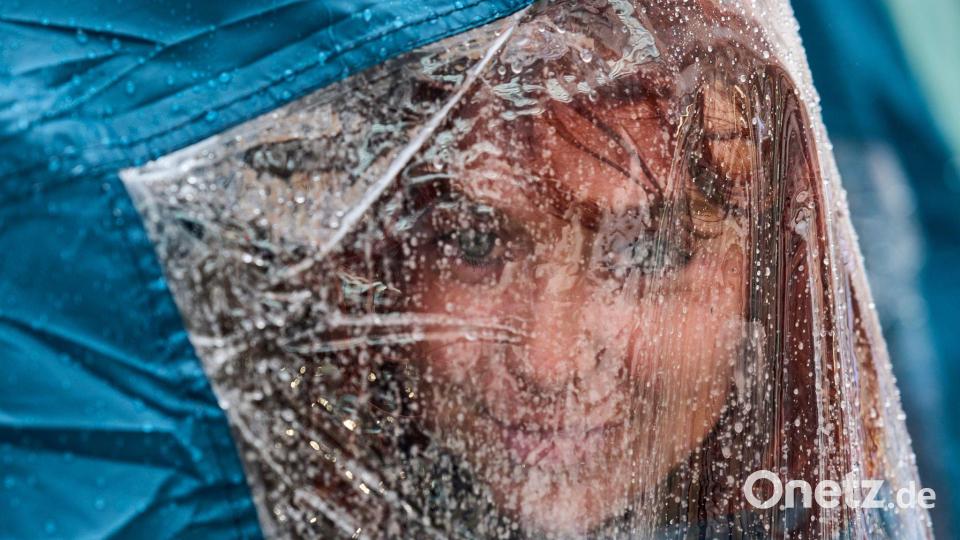 Eine Aktivistin blickt unter ihrer Regenkappe hervor, während sie bei starkem Regen auf dem Platz Puerta del Sol in Madrid an einem Protestcamp für das Recht auf Wohnen teilnimmt. Bild: Manu Fernandez/AP/dpa
