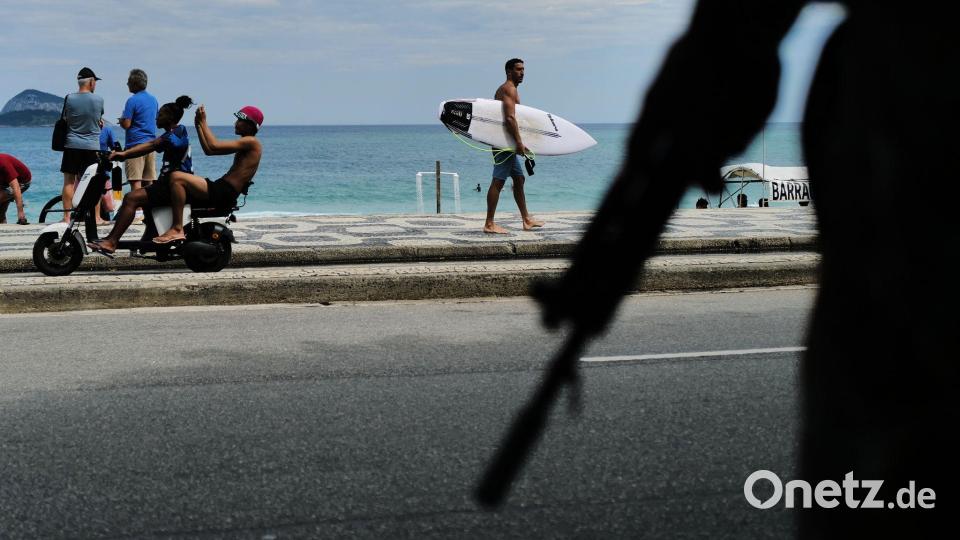 Ein Surfer spaziert am Strand von Leblon in Rio de Janeiro entlang, während Soldaten während der Präsidentenwahl in Brasilien auf dem gegenüberliegenden Bürgersteig Wache stehen. Bild: Lucas Landau/AP/dpa