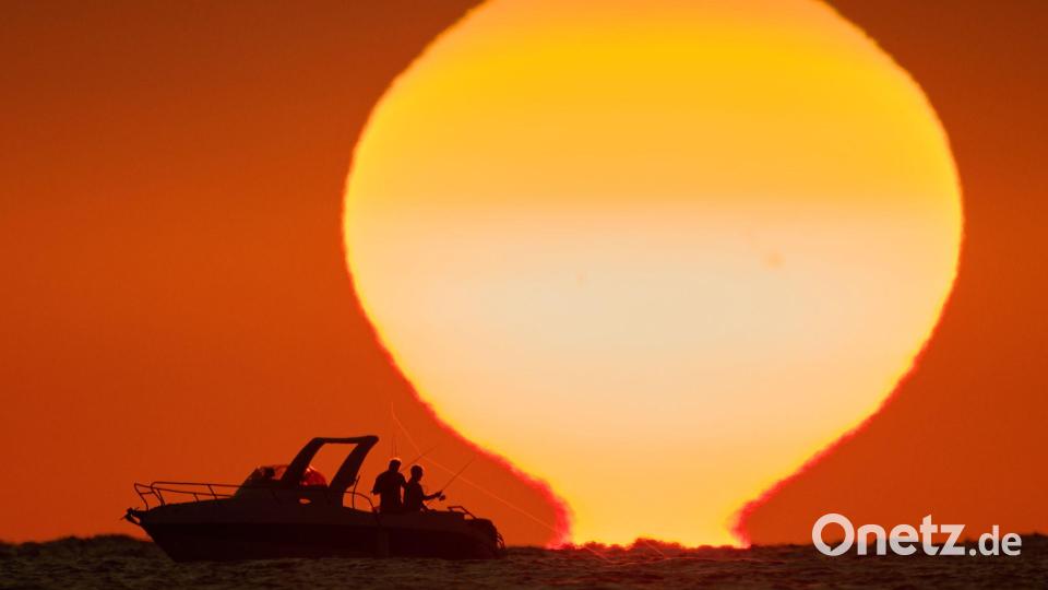 Fischer zeichnen sich als Silhouetten auf einem Boot ab, während die Sonne im Libanon über dem Mittelmeer untergeht. Bild: Hassan Ammar/AP/dpa