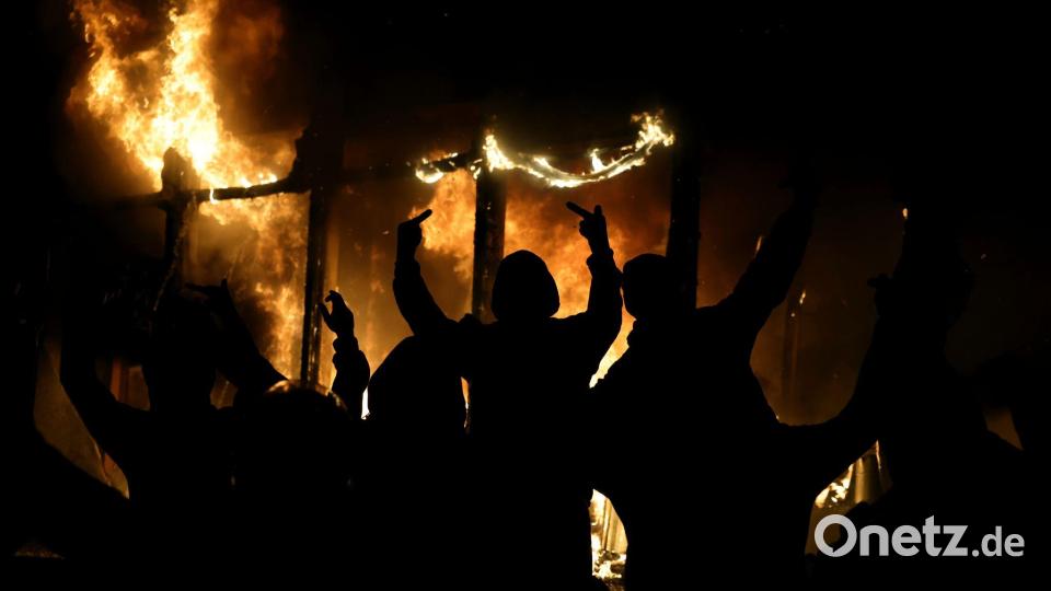 Ein vermummter Demonstrant streckt den Mittelfinger aus. Bild: Hameraldi Agolli/AP/dpa