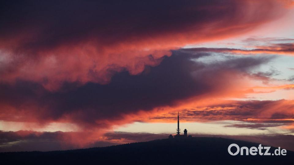 Vom Sonnenaufgang rötlich verfärbt zeigt sich der Himmel über dem Brocken in Sachsen-Anhalt. Bild: Julian Stratenschulte/dpa